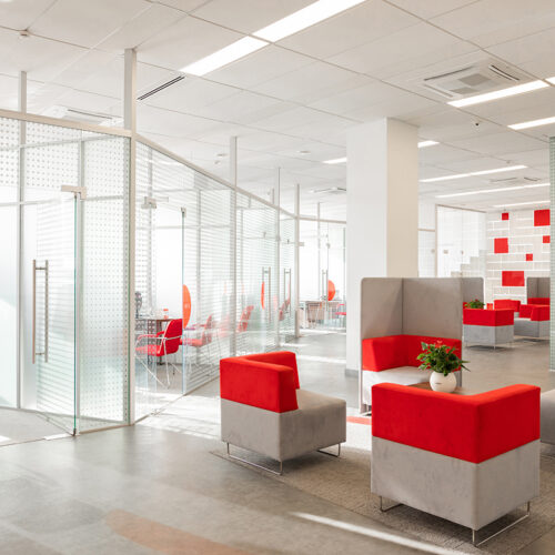 Minsk, Belarus - May 23, 2019: Corner of modern office with white walls, gray floor, open space area with red-white armchairs and rooms behind glass wall Commercial
