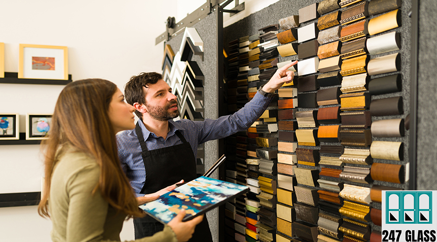Attractive salesman and pretty woman in her 20s are in a store and looking at a wall full of frame samples