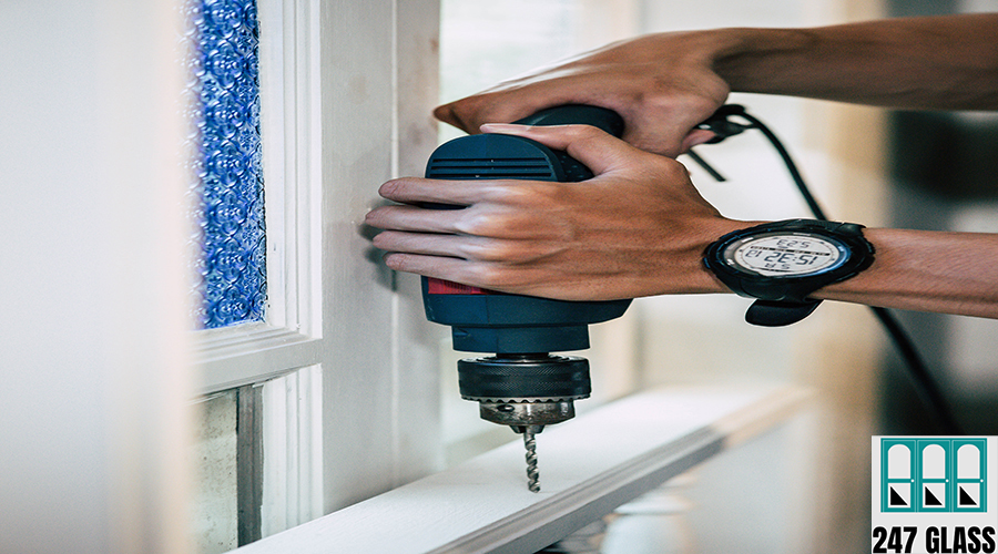 The carpenter holds the drill and drills the window. Selective focus.