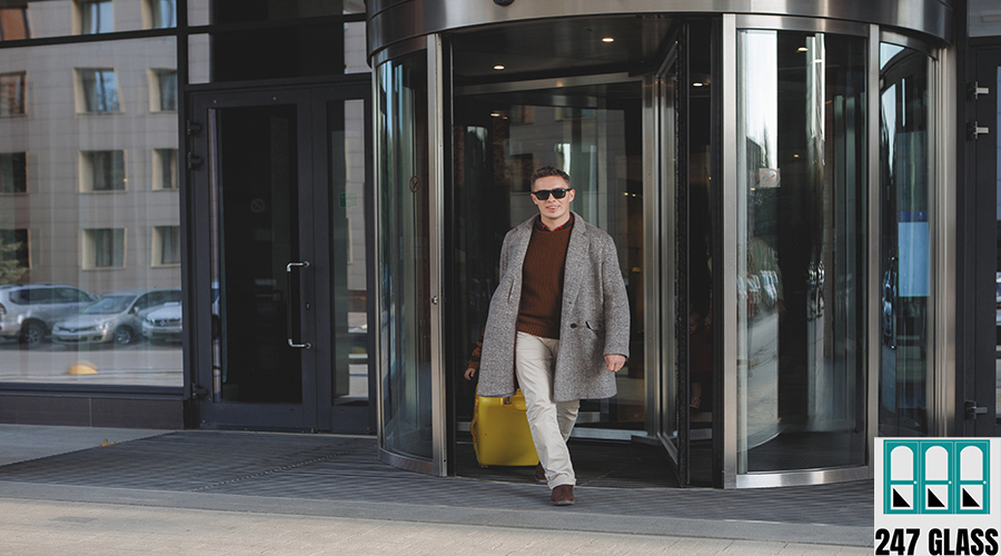 Man in black glasses, with a yellow suitcase in beige trousers, in a gray coat, leaves the hotel.