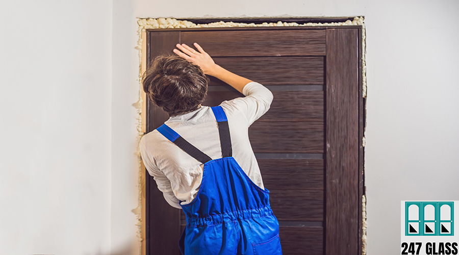 Young handyman installing door with an mounting foam in a room.