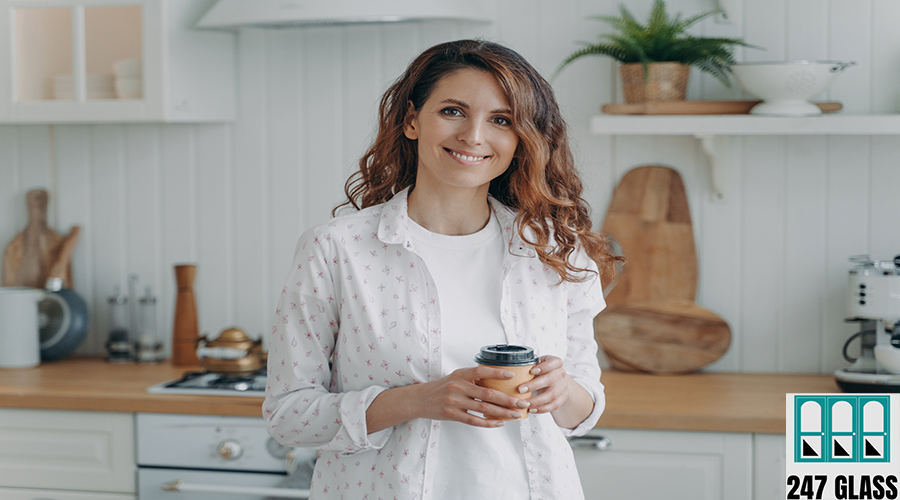 Smiling hispanic woman with paper cup of coffee standing in cozy modern kitchen, looking at camera glass replacement