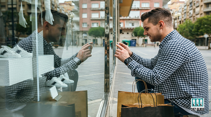 Young man taking a photo of a mannequin from a shop window of a fashion store